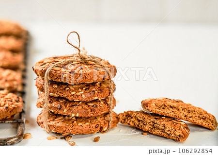 Homemade oatmeal cookies. Cookies with flax and sesame seeds on a white background. Selective focus on a stack of baked cookies tied with twine, sweetness as a gift. Festive baked goods 106292854