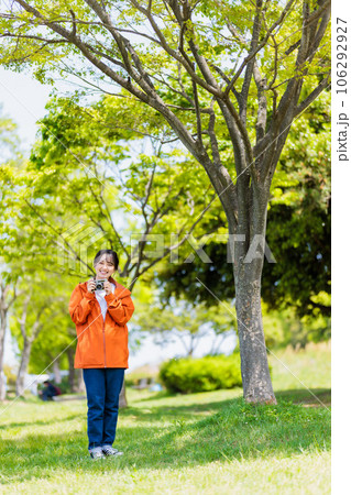 緑が美しい公園で写真を撮るカメラ女子 106292927