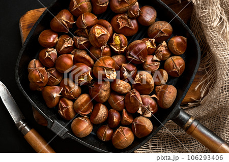 Fried chestnuts in a pan on a wooden stand, flat lay. Fresh roasted chestnuts for christmas or holidays, seasonal dish 106293406