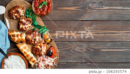 Fried meat. Meat balls or cutlets - Turkish kofte made from lamb and beef with cheese and spices. On a wooden platter with grilled vegetables, herbs and sauce. Layout with copy space Fried meat. Meat balls or cutlets - Turkish kofte made from lamb and beef with cheese and spices. On a wooden platter with grilled vegetables, herbs and sauce. Layout with copy space 106293574