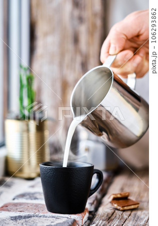 Hot milk is poured into a cup of coffee. Steam rises above the cup. Close-up selective focus on a cup of coffee Hot milk is poured into a cup of coffee. Steam rises above the cup. Close-up selective focus on a cup of coffee 106293862