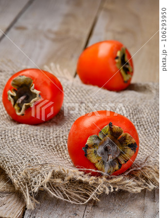 Ripe delicious orange persimmons. Fresh persimmon on a matting mat, close-up. Wooden rustic table, vertical frame. 106293950