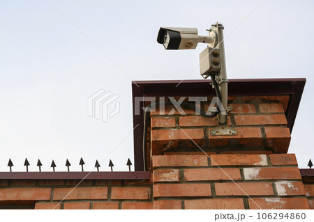 Closed-circuit television camera on a brick wall with iron spikes 106294860