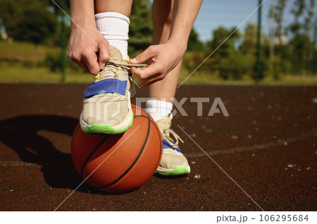 Closeup basketball player tying laces on training sneakers putting foot on ball 106295684