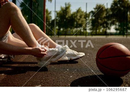 Cropped image of sportsman tying shoelaces sitting on basketball court 106295687