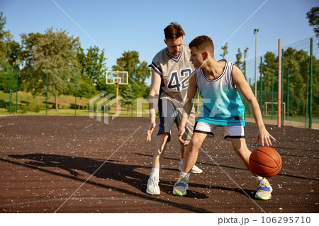 Young trainer teaching teenage boy playing basketball on street court Young trainer teaching teenage boy playing basketball on street court 106295710