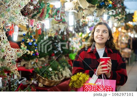 Girl walking in colorful Christmas street market, holding paper cup of warm mulled wine 106297101