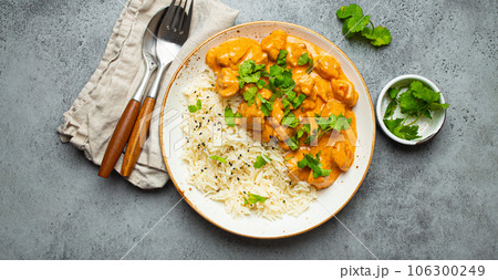 Traditional Indian dish chicken curry with basmati rice and fresh cilantro on rustic white plate on gray concrete table background from above. Indian dinner meal Traditional Indian dish chicken curry with basmati rice and fresh cilantro on rustic white plate on gray concrete table background from above. Indian dinner meal 106300249
