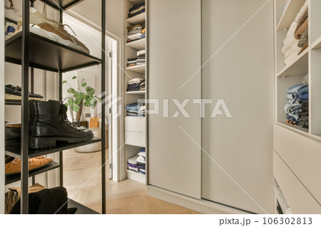 a walk - in closet with lots of clothes and shoes hanging on the wall behind it is an open white door a walk - in closet with lots of clothes and shoes hanging on the wall behind it is an open white door 106302813