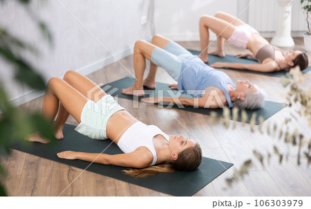 Women three generations doing different yoga exercises lying on back Women three generations doing different yoga exercises lying on back 106303979