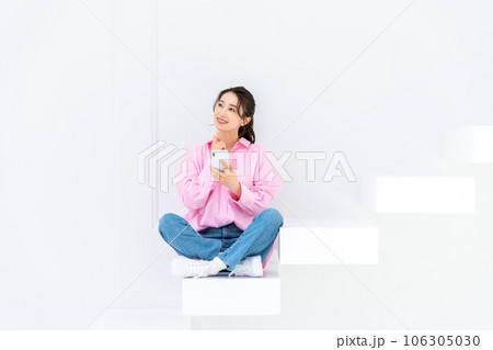 階段でスマホを見る若い女性 106305030