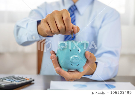 Businessman hand putting coin into blue piggy bank, saving money for future investment plan and retirement fund concept 106305499