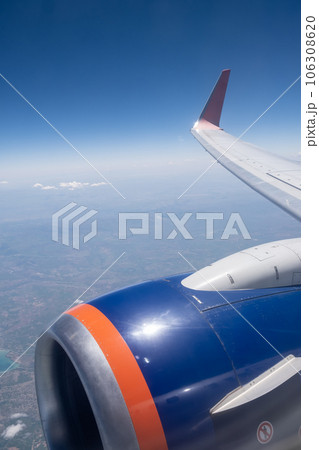 Airplane flight. Wing of an airplane flying above the clouds. View from the window of the plane. Airplane, Aircraft. Traveling by air. Aircraft's wing and land seen through the illuminator.  106308620