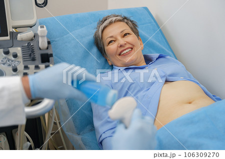 Middle aged woman patient lying on bed and having ultrasound examination of abdomen in clinic 106309270