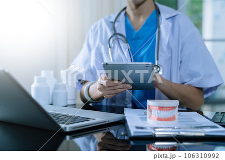 Dentist sitting at table with jaw samples tooth model and working with tablet and laptop in dental office professional dental clinic. medical doctor working.Dentist sitting at table with jaw samples 106310992
