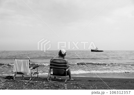 Man sitting on chair is watching an old ship sailing on sea 106312357