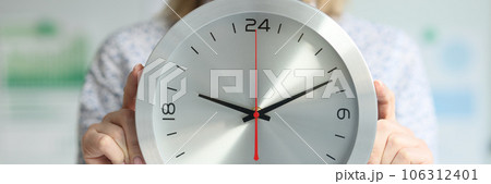 A woman in the office holds a wall clock, a close-up 106312401