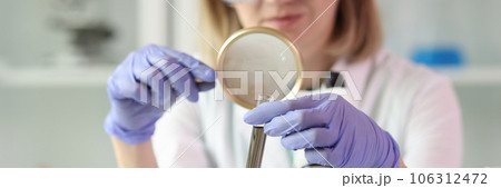A woman looks through a magnifying glass at a test tube A woman looks through a magnifying glass at a test tube 106312472