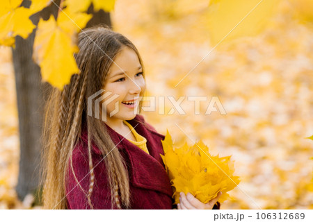 Dreamy cute little girl in autumn clothes in a park with yellow leaves. A smiling child is playing in the park. 106312689
