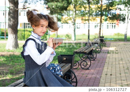 Girl with backpack eating sandwich packed in a sandwich box near school. A quick snack with a bun, unhealthy food, lunch from school. Back to school. Education, primary school classes, September 1 106312727