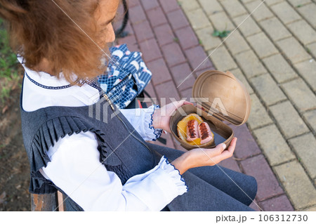 Girl with backpack eating sandwich packed in a sandwich box near school. A quick snack with a bun, unhealthy food, lunch from school. Back to school. Education, primary school classes, September 1 Girl with backpack eating sandwich packed in a sandwich box near school. A quick snack with a bun, unhealthy food, lunch from school. Back to school. Education, primary school classes, September 1 106312730