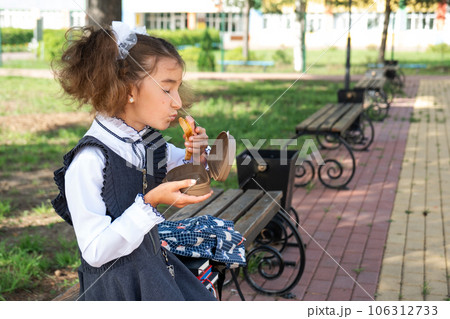 Girl with backpack eating sandwich packed in a sandwich box near school. A quick snack with a bun, unhealthy food, lunch from school. Back to school. Education, primary school classes, September 1 Girl with backpack eating sandwich packed in a sandwich box near school. A quick snack with a bun, unhealthy food, lunch from school. Back to school. Education, primary school classes, September 1 106312733