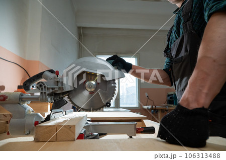 The master cuts the board with a circular saw in the workshop. Close-up of a carpenter's male hands at work. 106313488