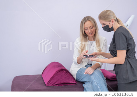 Eyelash extension master shows examples to a client. Woman choosing type of eyelash extension. Eyelash extension master shows examples to a client. Woman choosing type of eyelash extension. 106313619