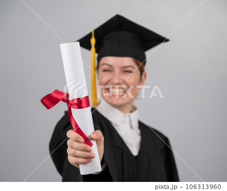 Emotional woman in graduate gown holding diploma in foreground.  Emotional woman in graduate gown holding diploma in foreground.  106313960