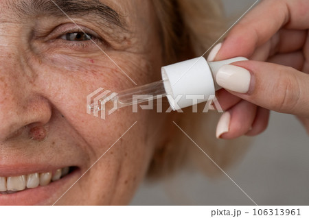 Close-up portrait of an old woman applying hyaluronic acid serum with a pipette. Anti-aging face care.  Close-up portrait of an old woman applying hyaluronic acid serum with a pipette. Anti-aging face care.  106313961