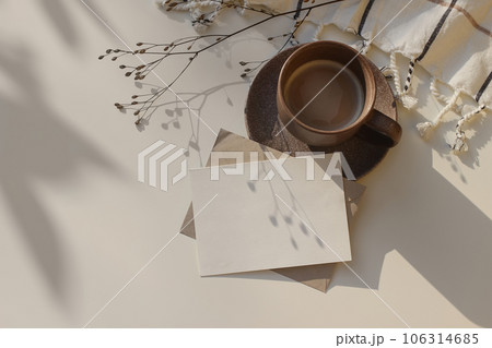 Winter still life. Blank Christmas greeting card, invitation mockup with dry flower in sunlight, shadows. Cup of coffee and white checkered plaid on table. Flatlay, top view. Copy space, no people 106314685