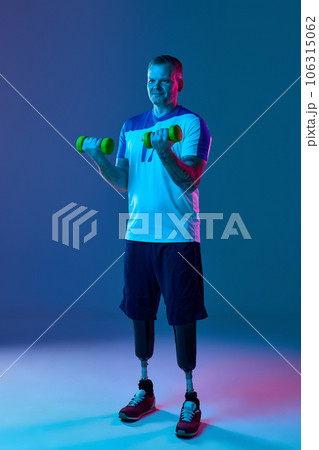 Young muscular man with prosthetic legs is training in gym with dumbbells in neon light. Motivation poster. Young muscular man with prosthetic legs is training in gym with dumbbells in neon light. Motivation poster. 106315062