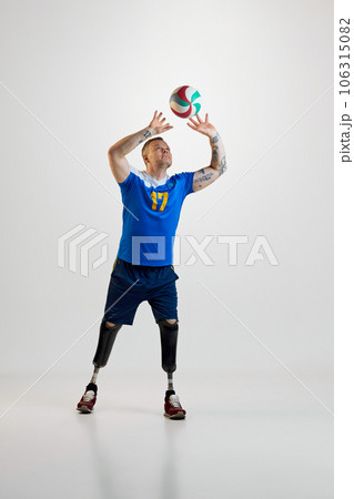 Confident young man with prosthetic legs disability in uniform hits volleyball ball in motion. Inclusive sport for people with disabilities 106315082