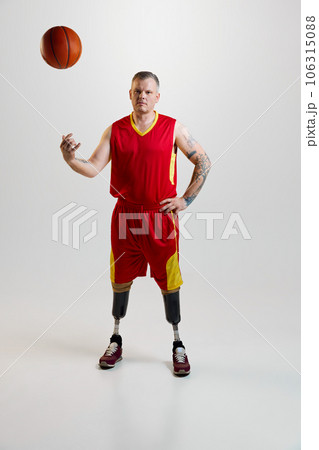 Confident, sporty man with prosthetic legs, disability in uniform throws up basketball ball. Inclusive sport for people with disabilities. Confident, sporty man with prosthetic legs, disability in uniform throws up basketball ball. Inclusive sport for people with disabilities. 106315088
