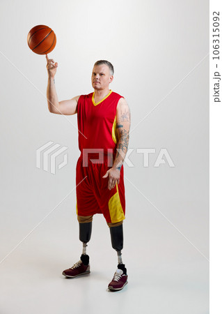 Attractive, confident, sporty man with prosthetic legs, disability in uniform spins basketball ball on finger. Inclusive sport for people with disabilities. Attractive, confident, sporty man with prosthetic legs, disability in uniform spins basketball ball on finger. Inclusive sport for people with disabilities. 106315092