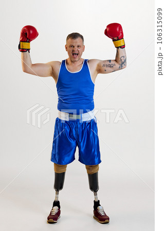 Full length of attractive confident man with prosthesis in boxing uniform shouting with raising hands and enjoying his hobby. Full length of attractive confident man with prosthesis in boxing uniform shouting with raising hands and enjoying his hobby. 106315099
