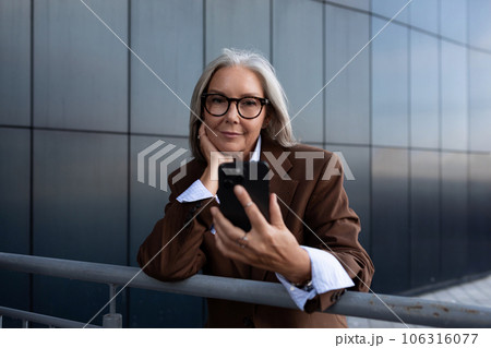 successful slender gray-haired mature business lady is dressed in a stylish brown jacket on the 106316077