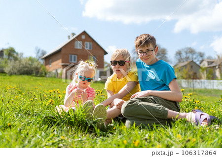 Happy childhood. Child siblings sits on dandelions filed on house background. Summer vacation time 106317864