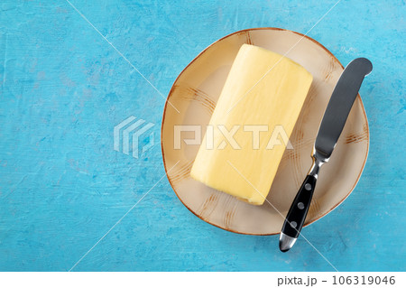 A stick of butter with a knife on a plate, top shot on a blue background A stick of butter with a knife on a plate, top shot on a blue background 106319046