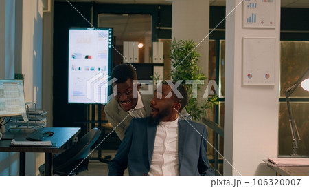 Businessman playing prank on unsuspecting coworker at work, pushing his desk chair. Relaxed staff personnel having fun during nightshift in office, taking break from work 106320007