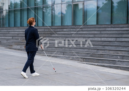 Blind businesswoman walking with tactile cane to business center. Blind businesswoman walking with tactile cane to business center. 106320244