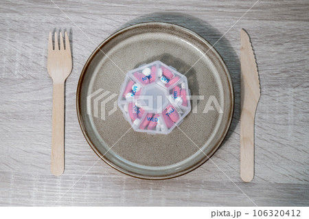 Organizer weekly shots with fork and knife medical pill box with doses of tablets for daily take medicine with white pink drugs and capsules. Daily vitamins at home. Health care and diseases cure 106320412