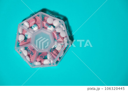Organizer weekly shots on blue background with Copy space for your text. Closeup of medical pill box with doses of tablets for daily take medicine with white pink drugs and capsules. Daily vitamins at 106320445