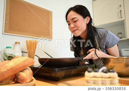 Attractive asian housewife making pancakes on frying pan, preparing breakfast in cozy domestic kitchen Attractive asian housewife making pancakes on frying pan, preparing breakfast in cozy domestic kitchen 106320858