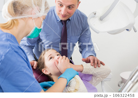 Frightened girl in dental chair refusing to open mouth Frightened girl in dental chair refusing to open mouth 106322458