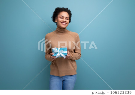 young happy latin woman with curly hair rejoices with a birthday present and isolated studio 106323839