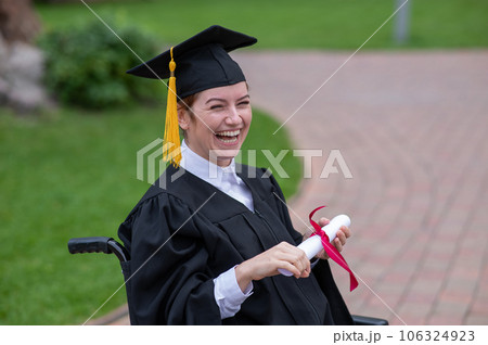 Happy caucasian woman in a wheelchair holding her diploma outdoors. 106324923