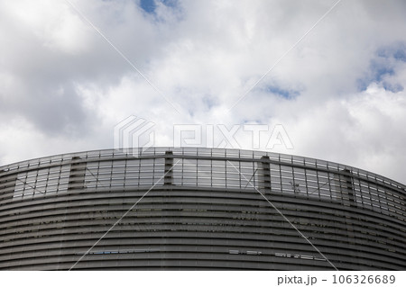 The modern facade of the sports hall against a sky with white clouds. The modern facade of the sports hall against a sky with white clouds. 106326689