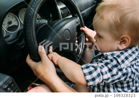 Dad shows his little son how to drive car while sitting behind wheel 106328323