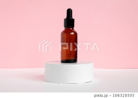 Amber glass dropper cosmetic bottles, white podium. Natural skin care SPA beauty product design. Mineral organic oil on pink background. Mock-Up. Oily pipette. Face and body treatment. Front view 106328505